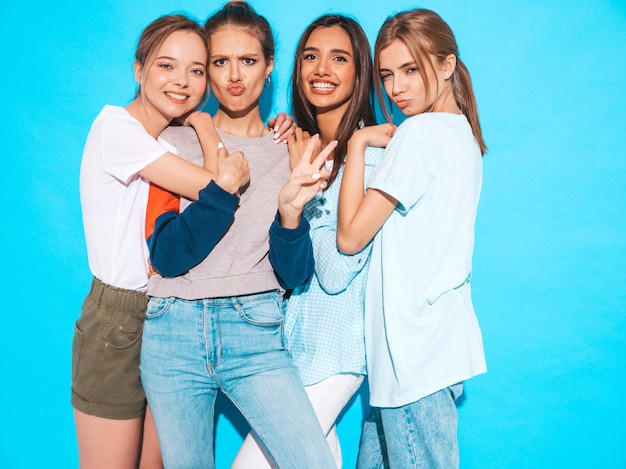 Free photo four young beautiful smiling hipster girls in trendy summer clothes. sexy carefree women posing near blue wall in studio. positive models having fun and hugging