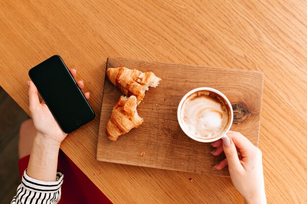 Frame above of a cup coffee with croissant on wood plate.