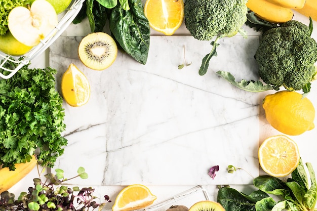 Free photo frame of ingredients for a green detox smoothie or a green salad of vegetables and fruits on a white marble background