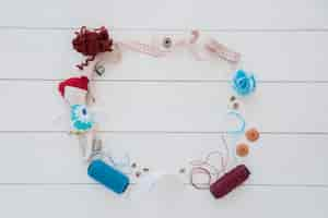 Free photo a frame made with rag doll; thimble; wool; measuring tape; button; ribbon and yarn spool on wooden desk