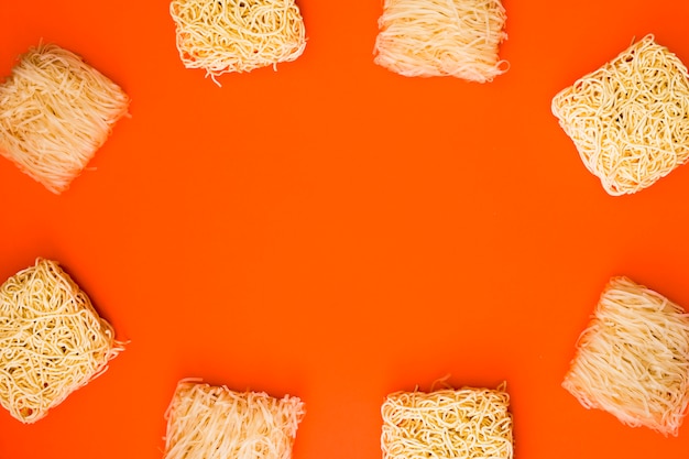 Free photo frame made with variety of raw noodle blocks over orange background