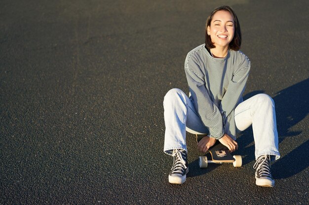 Freedom and happiness cute smiling asian girl sits on skateboard on sunny spring day happy laughing 