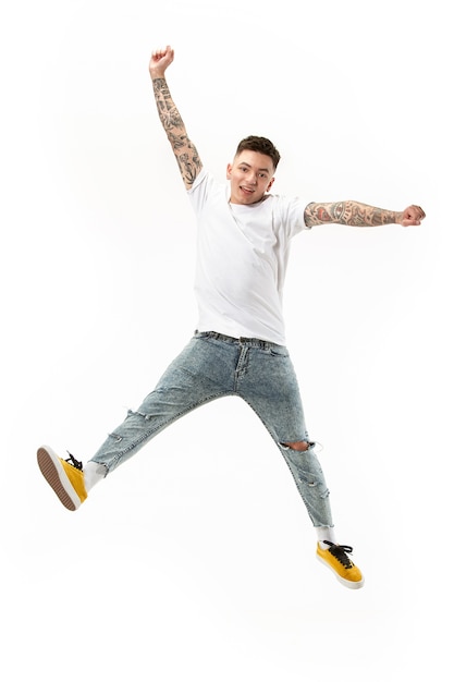 Free photo freedom in moving. mid-air shot of handsome happy young man jumping and gesturing against white studio background. running guy in motion or movement.