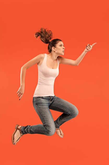 Freedom in moving. Mid-air shot of pretty happy young woman jumping and gesturing against orange studio background. Running girl in motion or movement.