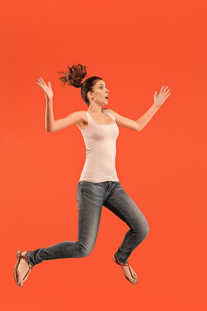 Freedom in moving. Mid-air shot of pretty happy young woman jumping and gesturing against orange studio background.