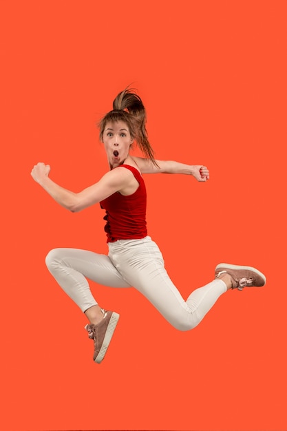 Freedom in moving. Mid-air shot of pretty happy young woman jumping and gesturing against orange studio background.