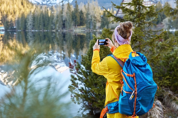 Freedom traveler takes pictures of scenic nature view, tries to capture beautiful lake with mountains and forest, stands back