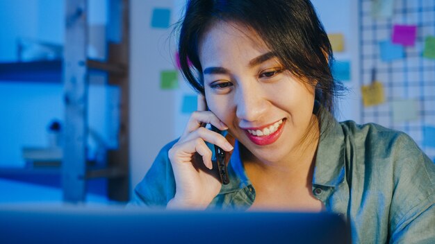 Freelance Asia women using laptop talk on phone busy entrepreneur working distantly in living room.