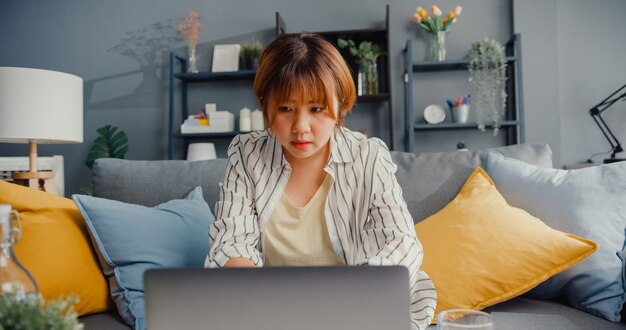 Freelance asian lady casual wear using laptop online learning in living room at house