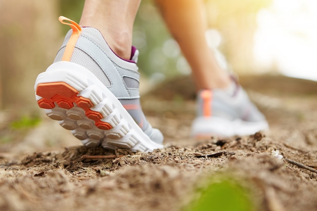 Free photo freeze action closeup of young woman walking or running on trail in forest or park in summer nature outdoors. athletic girl wearing sport shoes, exercising on footpath.