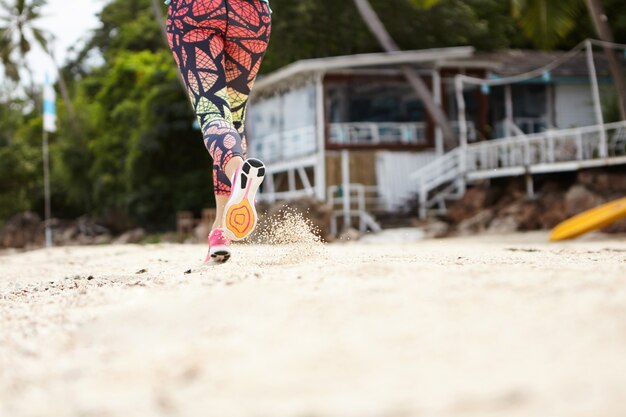 Freeze action shot of woman jogger in sportswear running on sandy beach on sunny day.