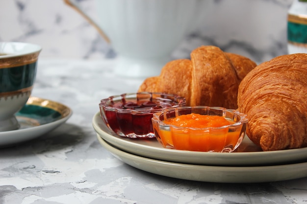 Free photo french breakfast with croissants, apricot jam, cherry jam and a cup of tea, red and yellow flowers