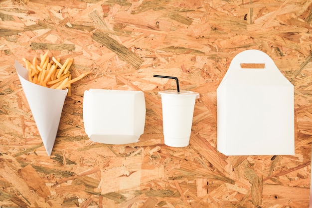 Free photo french fries; disposal cup and packages in a row on wooden table