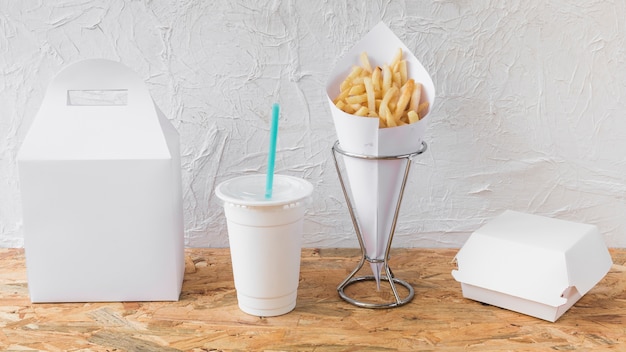 Free Photo french fries; disposal cup and packages on wooden desk