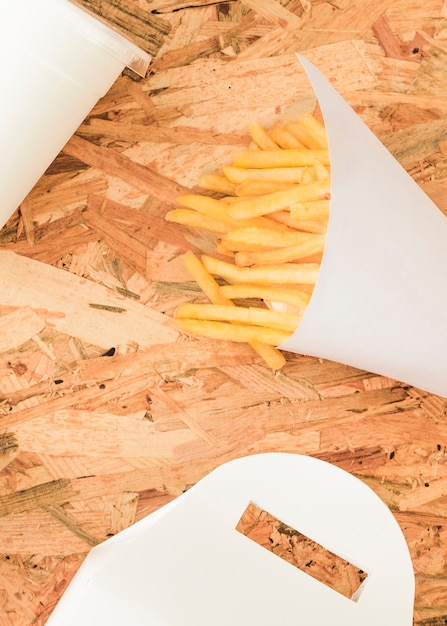 Free photo french fries in white cone on wooden textured backdrop