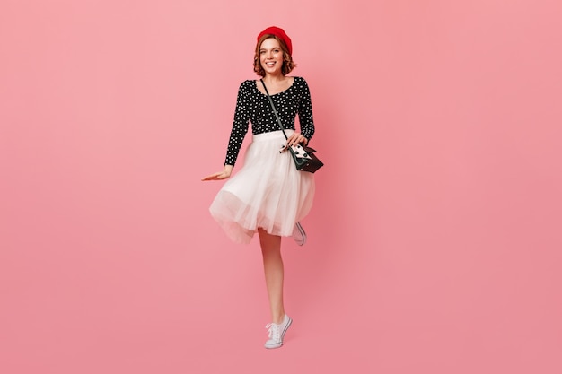 Free photo french lady with handbag dancing on pink background. full length view of wonderful girl in red beret and white skirt.