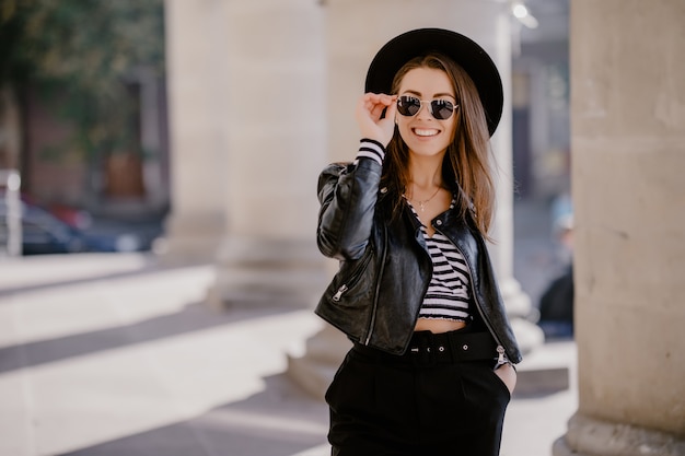 French pretty Young brown-haired girl in a leather jacket, black hat on the city promenade