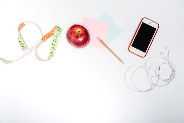 Free Photo fresh apple; measuring tape; adhesive notes and smartphone on white backdrop