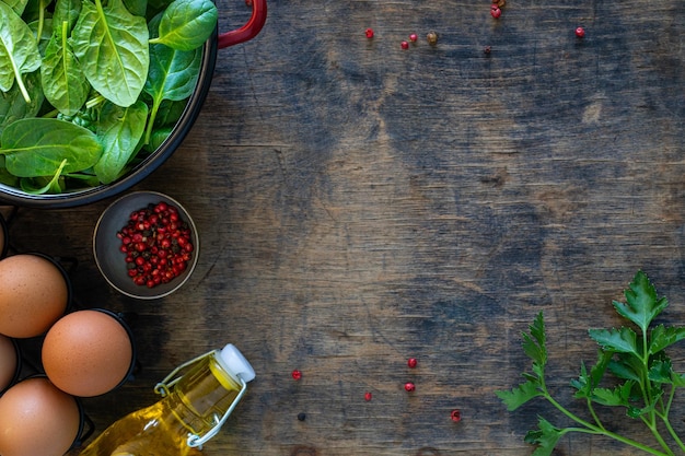 Fresh baby spinach leaves in a bowl and eggs on a wooden table Top view