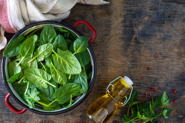 Fresh baby spinach leaves in a bowl and olive oil on a wooden table Top view