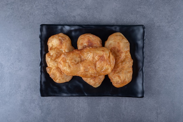 Fresh baked Russian pastry pirozhki on wooden plate on marble table.