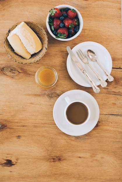 Fresh berries; bread; jam and coffee cup on wooden textured backdrop