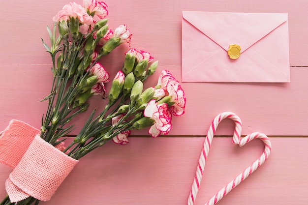 Free photo fresh bouquet of flowers with ribbon near envelope and candy canes