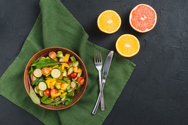 Free photo fresh bowl of vegetable salad; oranges and grapefruits on black concrete background