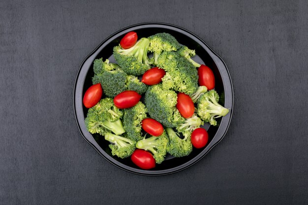 Fresh broccoli and cherry tomato in black bowl on black stone surface