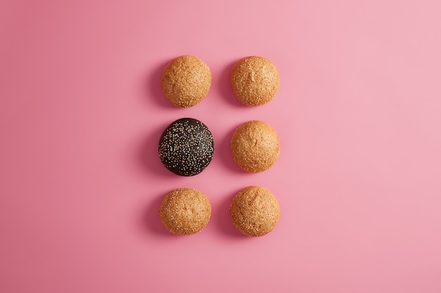 Fresh burger buns with sesame seeds arranged in two rows on rosy background. Preparing fast food or homemade hamburger. Food photography. Unhealthy eating or diet. Round soft brioches. Selective focus