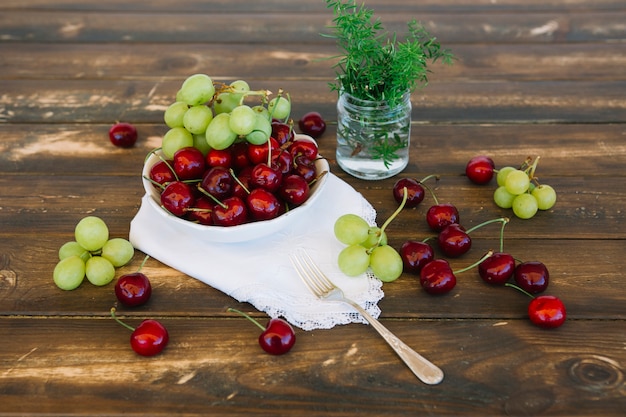 Free photo fresh cherries and grapes in bowl on wooden backdrop