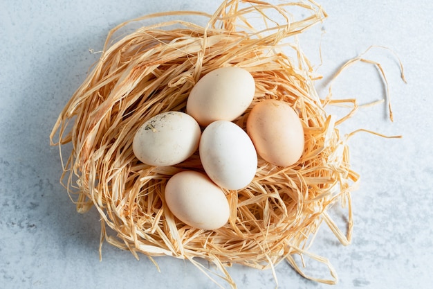 Fresh chicken eggs in straw over grey surface. 