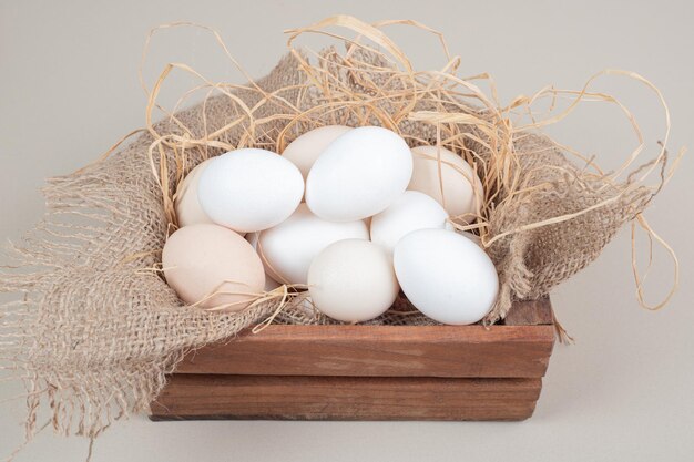 Fresh chicken white eggs with hay on wooden basket .