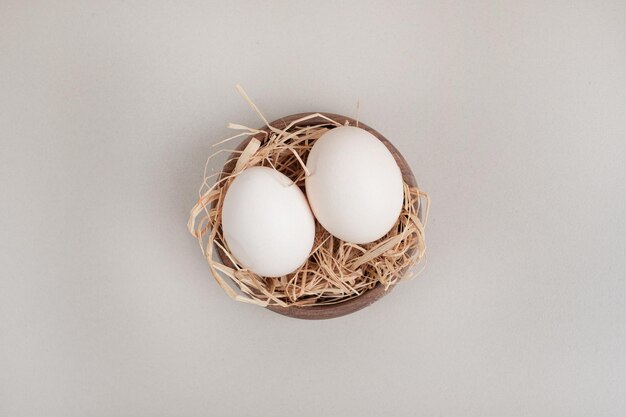 Fresh chicken white eggs with hay in wooden bowl.