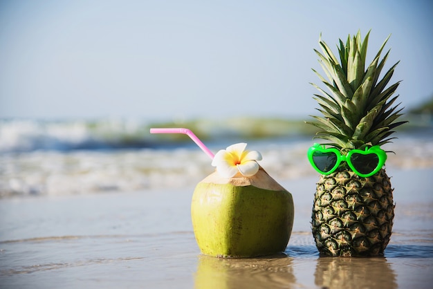 Free photo fresh coconut and pineapple put sun lovely glasses on clean sand beach with sea wave - fresh fruit with sea sand sun vacation concept