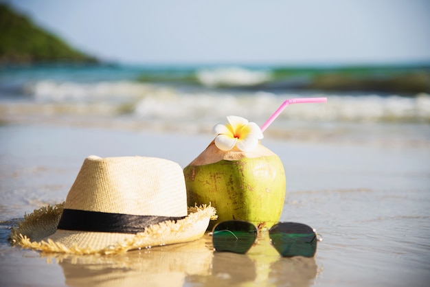 Free Photo fresh coconut with hat and sun glasses on clean sand beach with sea wave - fresh fruit with sea sand sun vacation concept