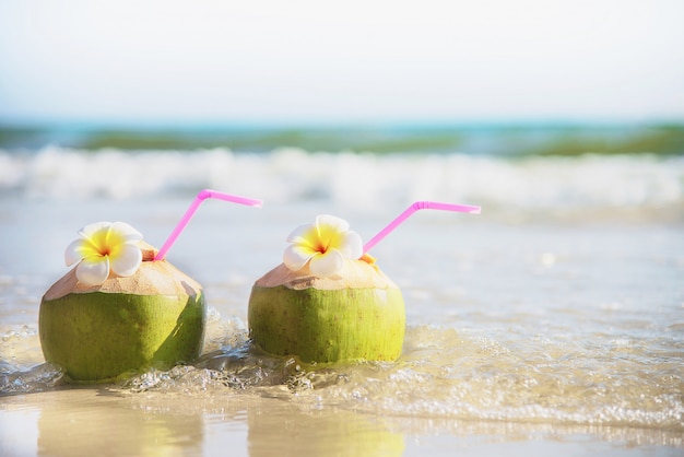 Fresh coconut with plumeria flower decorated on clean sand beach with sea wave - fresh fruit with sea sand sun vacation concept