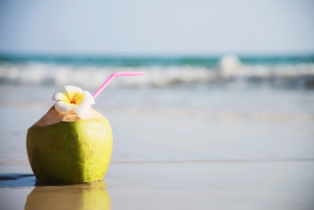 Fresh coconut with plumeria flower decorated on clean sand beach with sea wave - fresh fruit with sea sand sun vacation concept