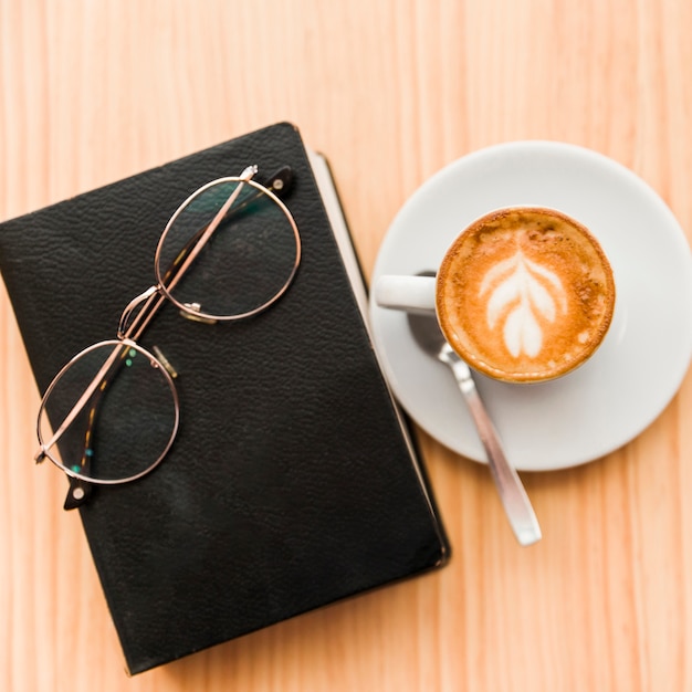 Fresh coffee latte with spectacles and book on wooden table