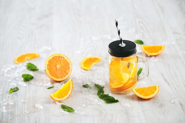 Free photo fresh cold summer lemonade from citrus and sparkling water in rustic jar with stripe straw isolated on wooden table.