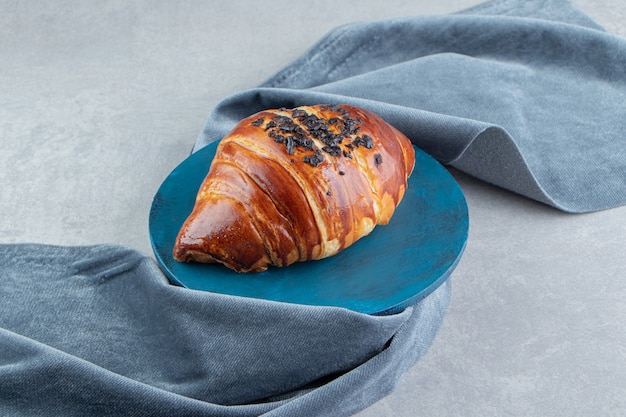 Fresh croissant decorated with drop chocolate on blue board. 