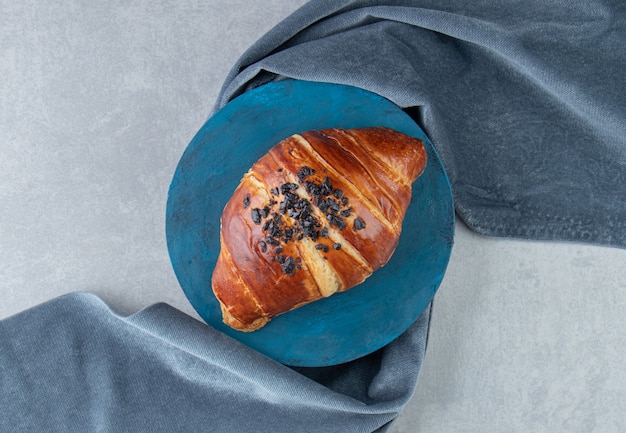 Fresh croissant decorated with drop chocolate on blue board. 