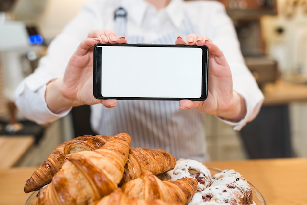 Fresh croissant in front of woman holding smart phone with blank white screen