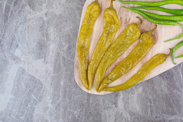 Fresh and fermented peppers on wooden board.