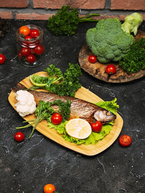 Fresh fish seabass and ingredients for cooking. Raw fish seabass with spices and herbs on black slate table. Top view.