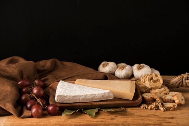 Free photo fresh food with garlic, cheese and grapes near brown cloth on table