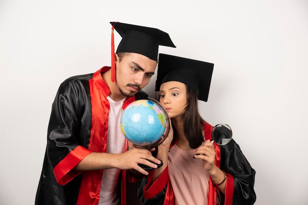 Free Photo fresh graduate students in gown looking at globe on white.