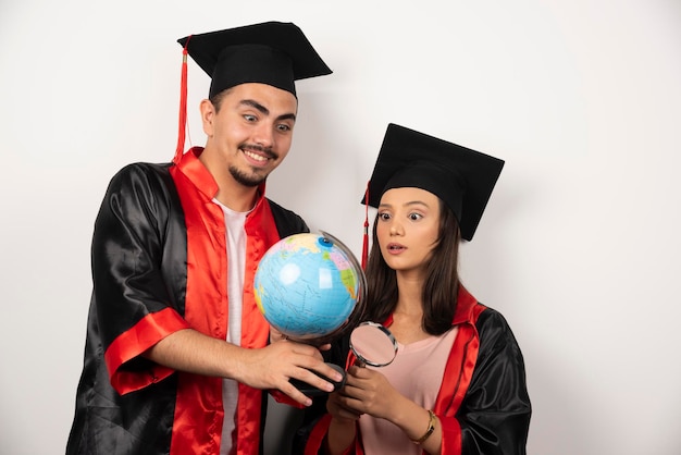 Free Photo fresh graduates in gown looking at globe on white.