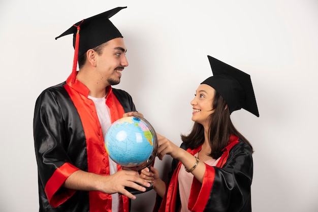 Free Photo fresh graduates in gown looking at globe on white.