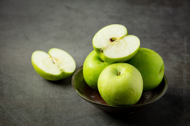 Fresh green apples cut in half put in black bowl on dark background